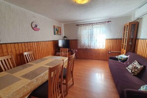 Une pièce comprenant une table à manger en bois, des chaises, un canapé, un téléviseur et une fenêtre avec des rideaux.