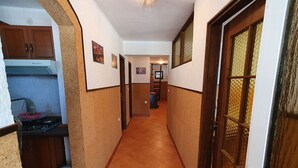 A narrow hallway with a kitchen on the left, a staircase in the center, and a door with a textured window on the right. - Holiday flat with panoramic view and barbecue on the terrace (Gradinje)