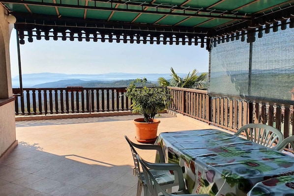 Un balcon abrité offrant une vue sur les montagnes lointaines, une plante en pot et une table avec des chaises.