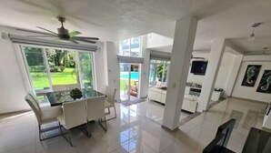 A spacious living area with a dining table, chairs, a ceiling fan, and a large sliding glass door leading to a garden. - Playacar Villa 10 pax ruins & beach (Playa del Carmen)
