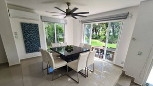 A dining area with a glass table and chairs, a ceiling fan, and large windows with a view of the outdoors. - Playacar Villa 10 pax ruins & beach (Playa del Carmen)