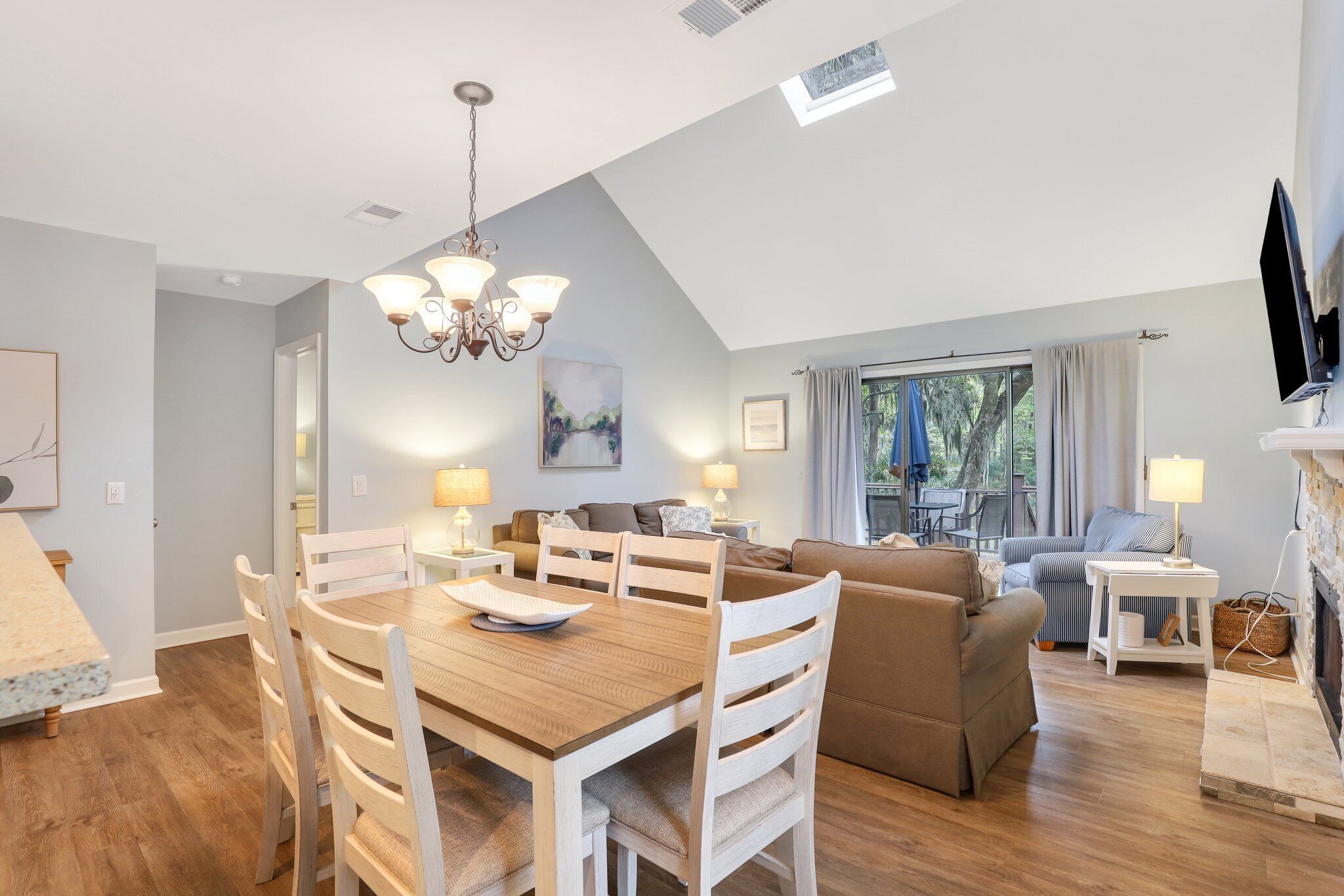A modern living room with a wooden dining table, white chairs, a sofa, and a TV.