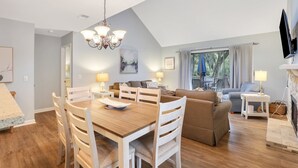 Ein modernes Wohnzimmer mit einem Holzesstisch, weißen Stühlen, einer Couch und einem Fernseher.