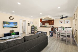 A modern living room with a grey sofa, a flat-screen TV, and a dining area with a table and chairs.