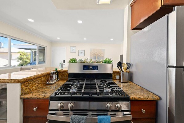 A modern kitchen with a gas stove, stainless steel appliances, granite countertops, and a refrigerator.