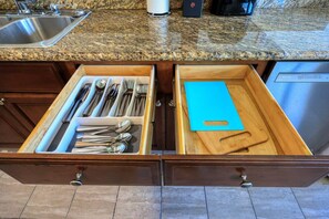 A kitchen drawer with utensils and a cutting board.