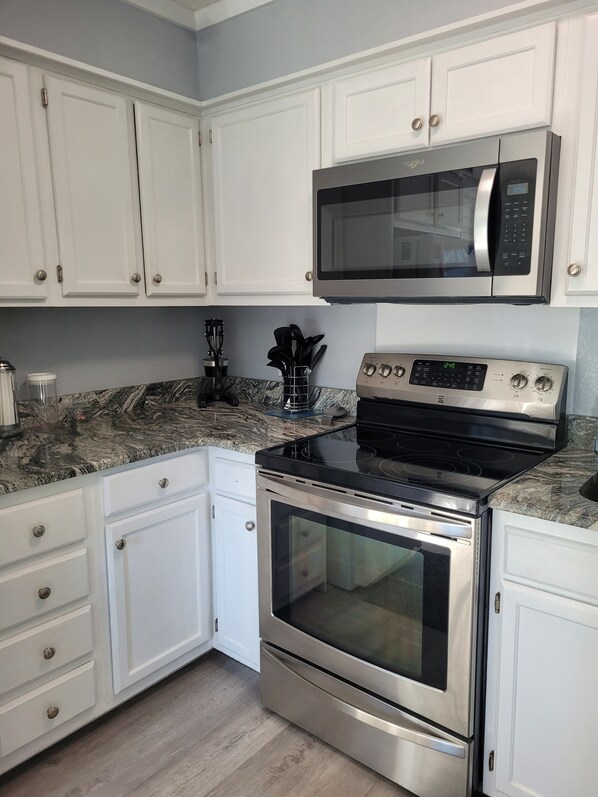A modern kitchen with white cabinets, a stainless steel microwave, a stove, and an oven.