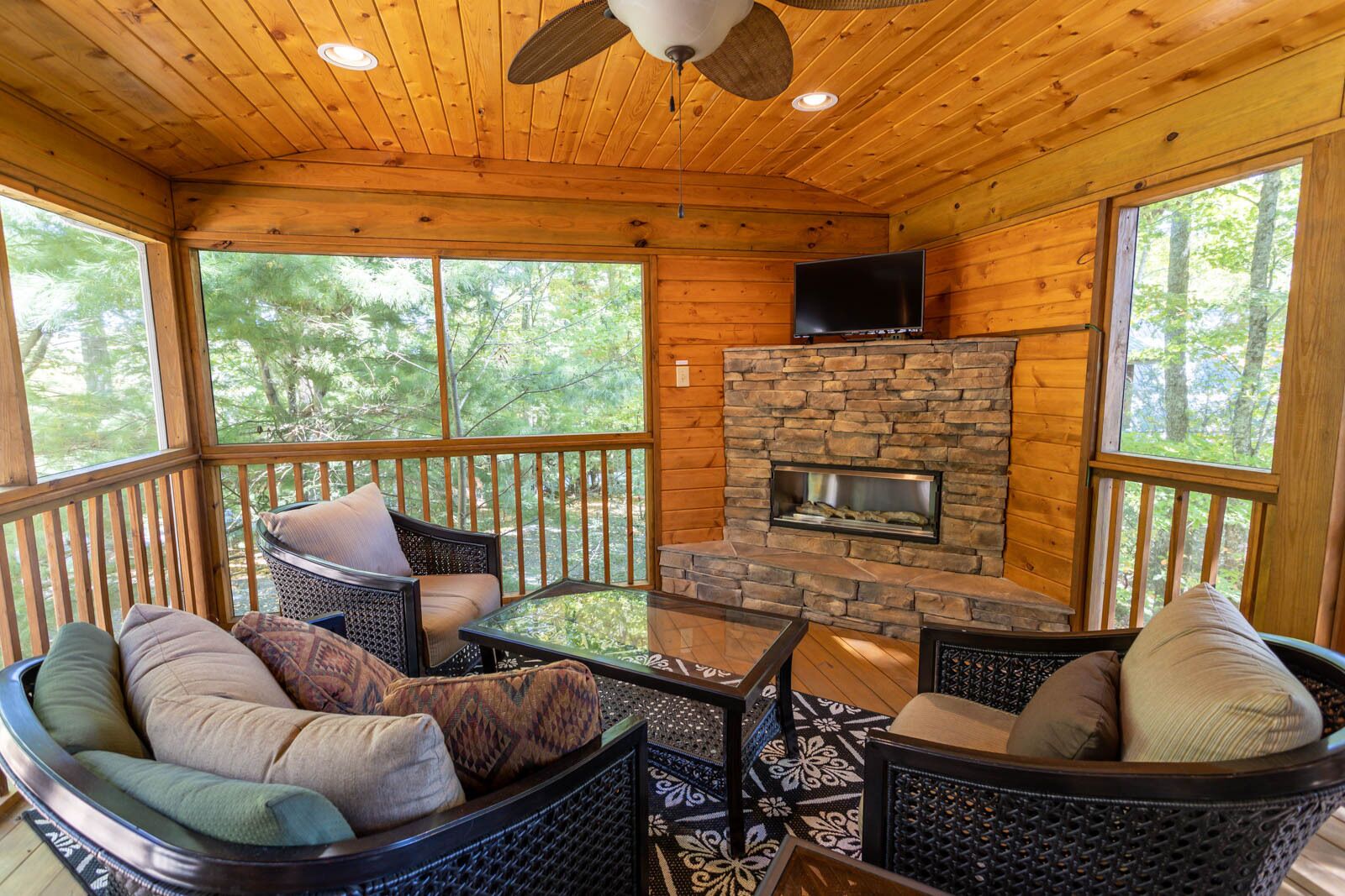 A wooden cabin with a stone fireplace, wicker furniture, and large windows.