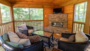 A wooden cabin with a stone fireplace, wicker furniture, and large windows.