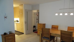 A dining area with a wooden table and chairs, a kitchen in the background, and a hallway leading to another room.