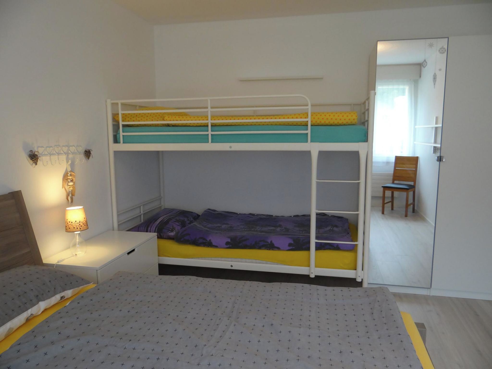 A bunk bed room with a desk and chair, a lamp, and a door leading to another room.