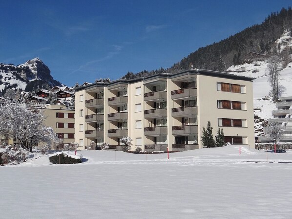 A multi-story hotel with balconies, surrounded by snow-covered trees and mountains.