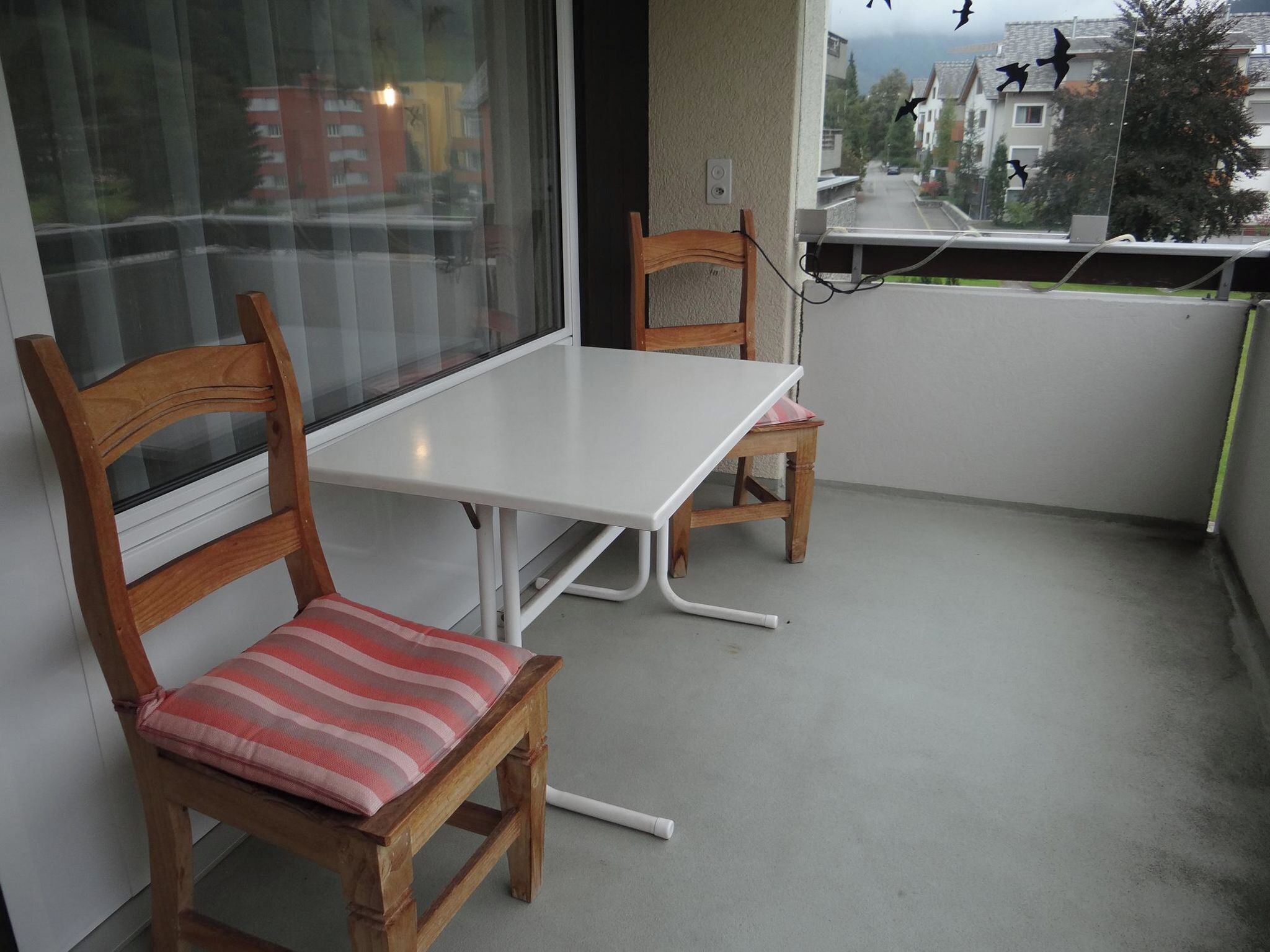 Un balcón con una mesa blanca y dos sillas de madera con cojines.