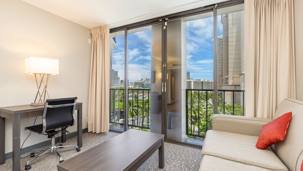 Une chambre d’hôtel moderne dotée d’une grande porte-fenêtre coulissante donnant sur un balcon, d’un bureau avec une chaise, d’un canapé et d’une lampe.