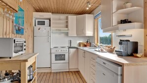 A compact kitchen with a microwave, stove, and dishwasher, wooden cabinets, and a window providing natural light.