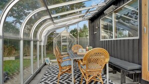 A greenhouse with a table and chairs, a bench, and a view of the garden.