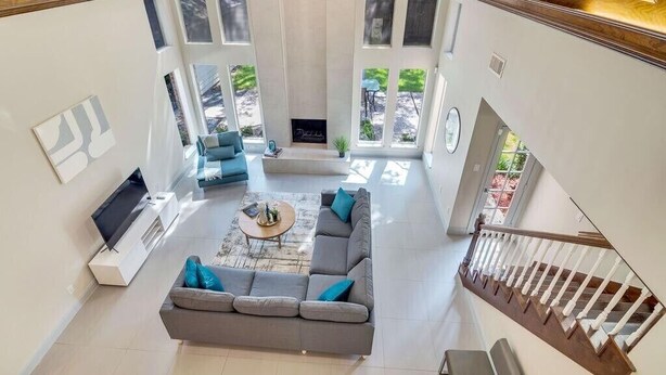 A spacious living area with a gray sofa, coffee table, and a TV. A staircase with a wooden railing leads to an upper level. - Modern 4BD in Katy TX (Katy)