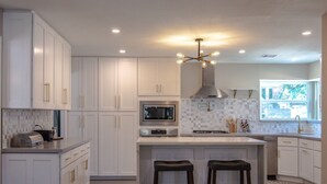 A modern kitchen with white cabinets, a central island with stools, a microwave, a gas stove, and a hanging light fixture. - Modern 4BD in Katy TX (Katy)