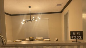 A kitchen with a dining table set for four, a bowl, and a sign that reads "WINE O'CLOCK". - Modern 4BD in Katy TX (Katy)