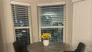 A round dining table with two black chairs, a white vase with yellow flowers, and a window with blinds. - Modern 4BD in Katy TX (Katy)