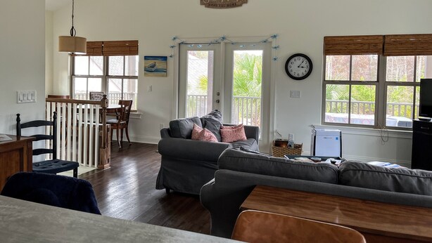 A spacious living room with a grey sofa, wooden dining table, and chairs. A ceiling fan and a clock are visible on the walls. - Peaceful European Cottage with (Ocala)