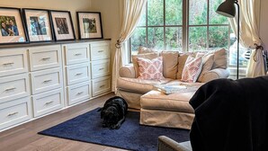 A living room with a sofa, a dog, a blue rug, a lamp, and framed pictures on a cabinet. - Peaceful European Cottage with (Ocala)