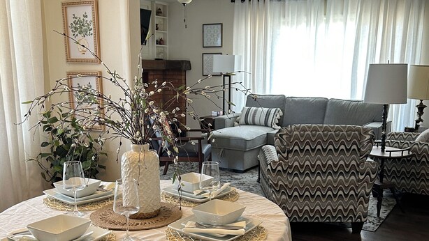A dining area with a round table set for four, surrounded by chairs. There is a fireplace in the background, and a sofa and armchair are visible in the living room area. - Charming bungalow in the heart of Southwest Colorado (Cortez)