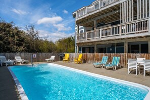 A swimming pool with lounge chairs, a wooden deck, and a two-story building with a balcony.