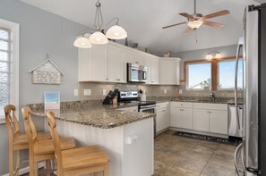 A kitchen with granite countertops, white cabinets, a built-in microwave, and a ceiling fan. - 123 Beach Therapy-Oceanside, private pool, hot tub, dog friendly, close to beach (Duck)