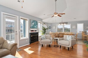 A spacious living room with a fireplace, a dining area with wooden chairs, and large windows allowing natural light.