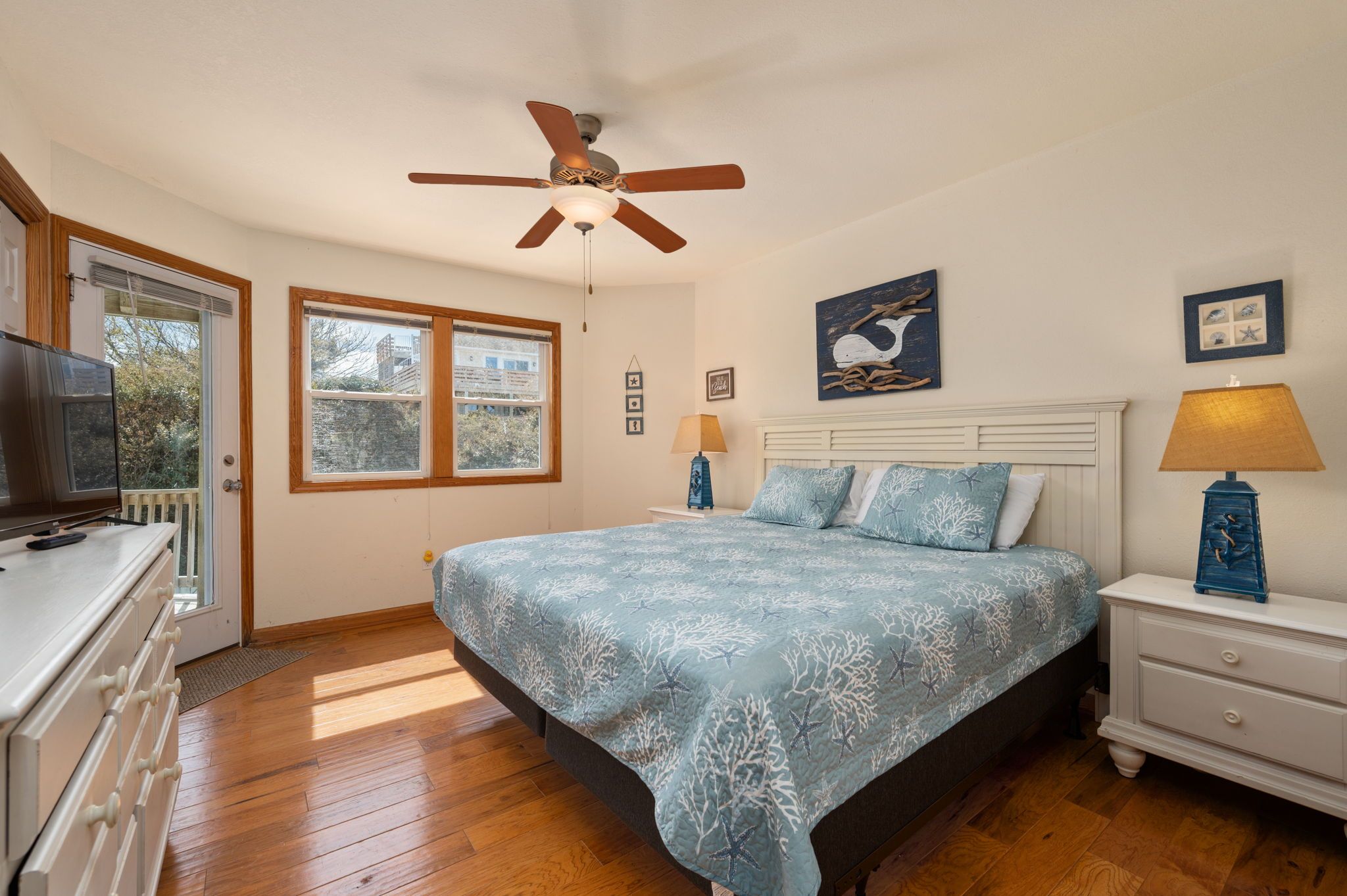 A bedroom with a bed, a ceiling fan, a nightstand, a lamp, a dresser, and a window.