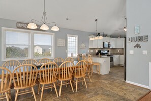 Une cuisine spacieuse avec des meubles blancs, un îlot central et un coin repas doté de chaises en bois.