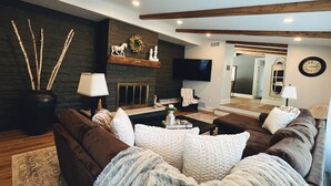 A modern living room with dark stone walls, wooden beams, a fireplace, a flat-screen TV, and a large mirror. -  HOT TUB and SAUNA at 'CHIC HIDEAWAY''  Paw Paw Lake Golf club across the street (Watervliet)