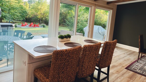 A modern kitchen with a large island, built-in bar stools, and large windows offering a view of the outdoor patio area. -  HOT TUB and SAUNA at 'CHIC HIDEAWAY''  Paw Paw Lake Golf club across the street (Watervliet)