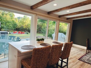 Una cocina moderna con una isla grande, taburetes integrados y ventanas amplias que ofrecen vistas del patio exterior.
