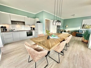 A modern kitchen with white cabinets, a wooden dining table, and pink upholstered chairs.