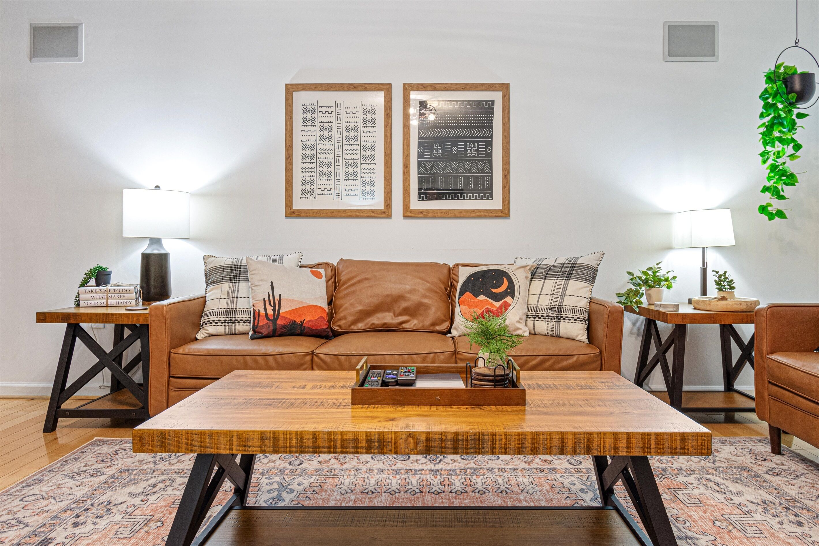 A living room with a brown leather sofa, two framed wall art pieces, a wooden coffee table, and two side tables with lamps and decorative items.