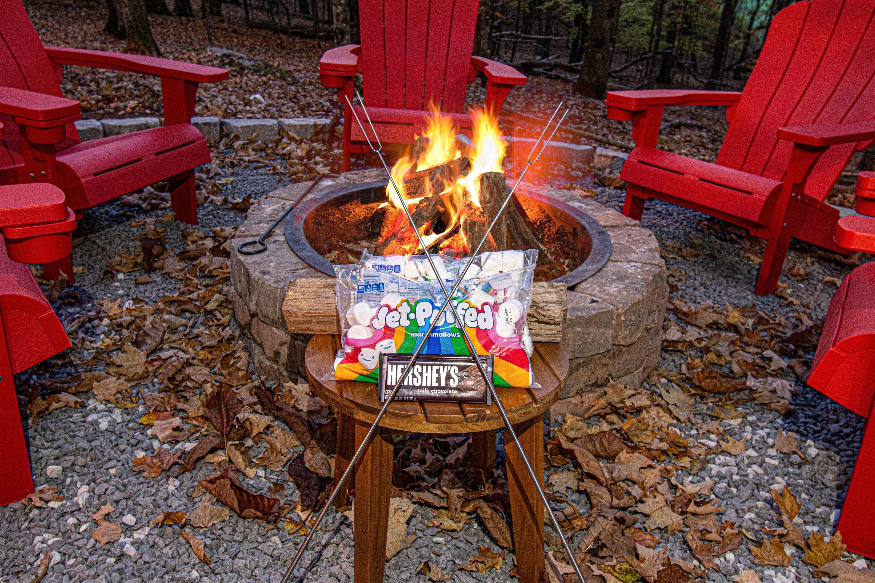 Een kampvuur met marshmallows en Hershey's chocolade, omringd door rode Adirondack stoelen.