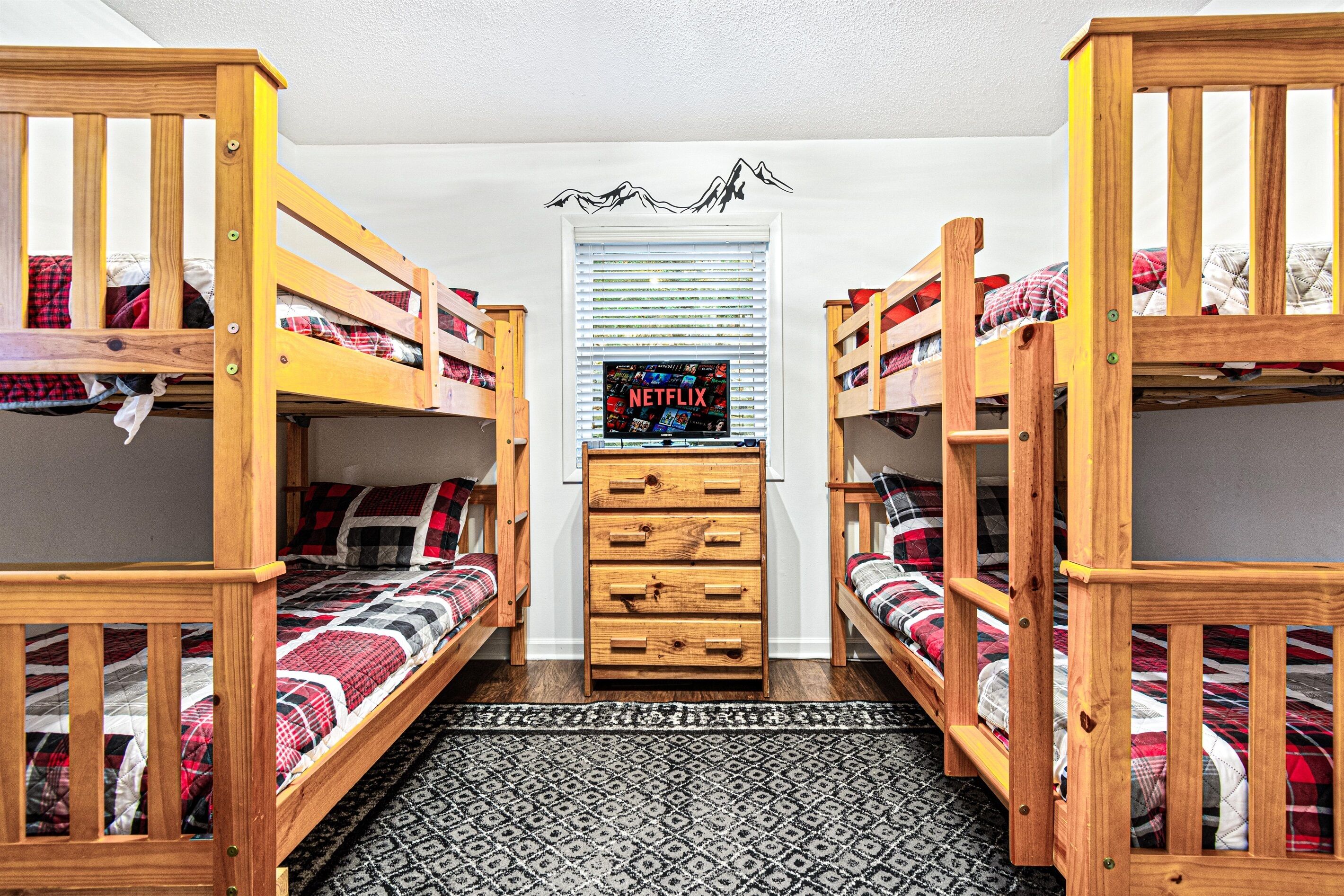 A room with three bunk beds, a wooden dresser, and a television displaying 'NETFLIX'.
