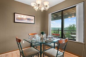 A dining area with a glass table, chairs, a chandelier, a framed painting, and a view of the outdoors.