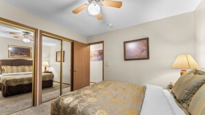 Una camera d'albergo con un letto, uno specchio, una ventola a soffitto, un comodino, una lampada e un quadro appeso al muro.