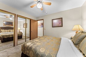 A hotel room with a bed, a mirror, a ceiling fan, a nightstand, a lamp, and a painting on the wall. - Newly Updated Condo w Gorgeous Table Rock View_Cmty Outdoor Pool_Near Sdc_Free Tickets (Branson)
