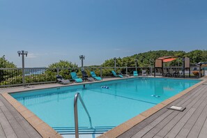 A rectangular swimming pool with a wooden deck, surrounded by lounge chairs and a fence.