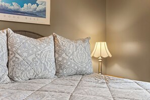 Una cama con almohadones estampados y un cabecero, una lámpara de noche y una obra de arte enmarcada en la pared.