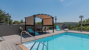 Una piscina con bordo in legno, lettini, zona relax coperta e vista sul paesaggio.