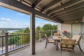 A covered outdoor area with a table and chairs, a grill, and a view of a lake and forest.
