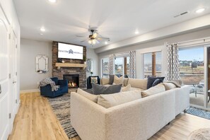 A modern living room with a fireplace, a ceiling fan, and a large window with a view.
