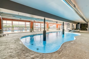 An indoor swimming pool with clear views of the outside, a stone wall, and a bar area.