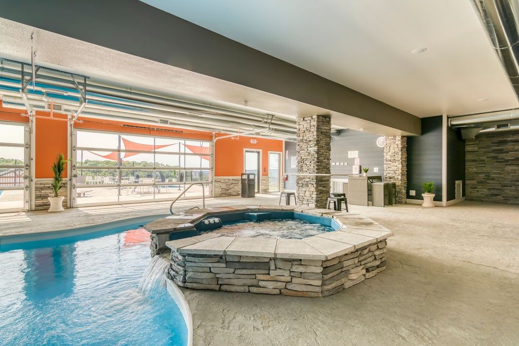 An indoor swimming pool with a hot tub, stone walls, and a view of the outdoors.
