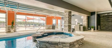 An indoor swimming pool with a hot tub, stone walls, and a view of the outdoors.